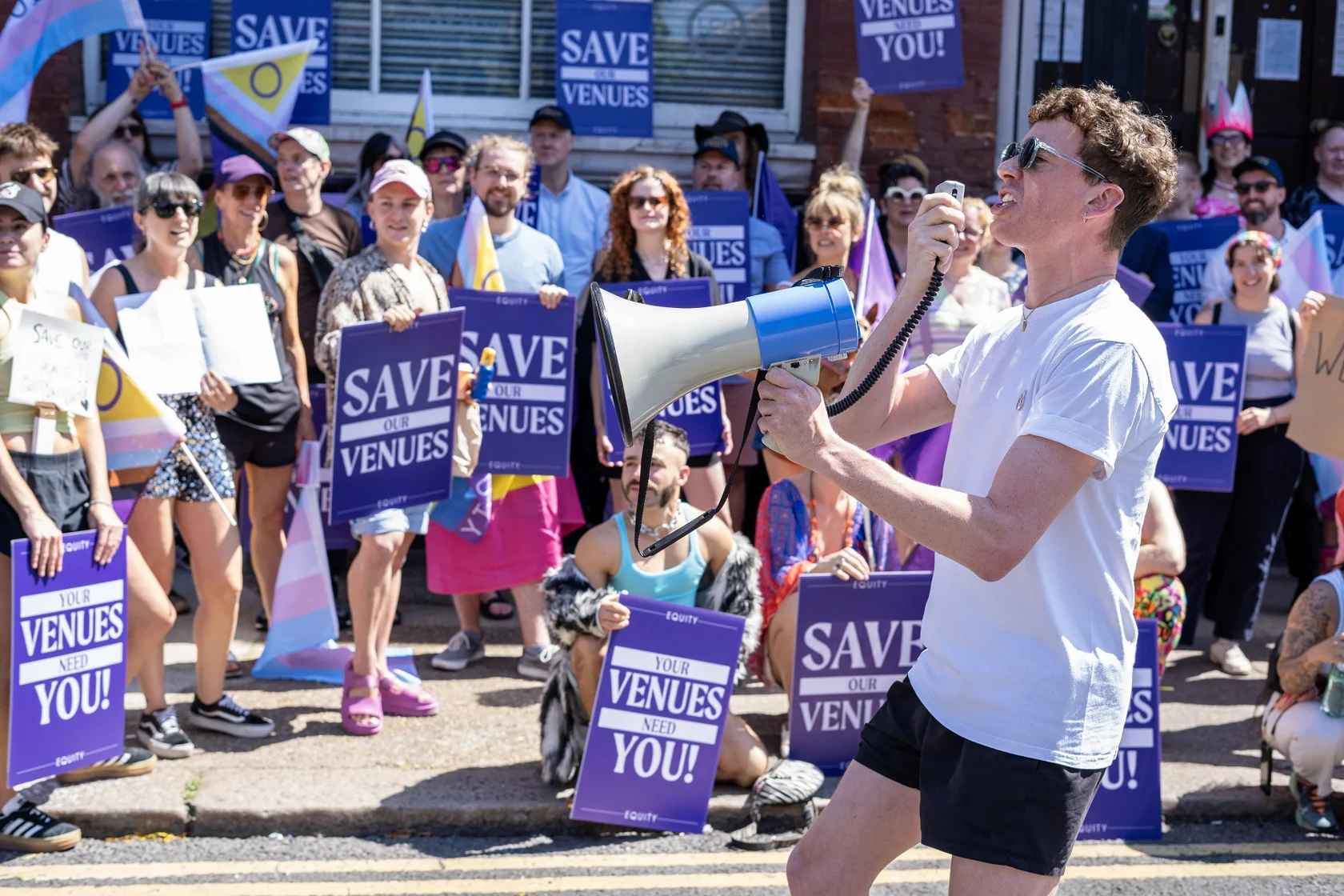 A person with megaphone addresses a rally with people holding signs saying "Your venues need you"
